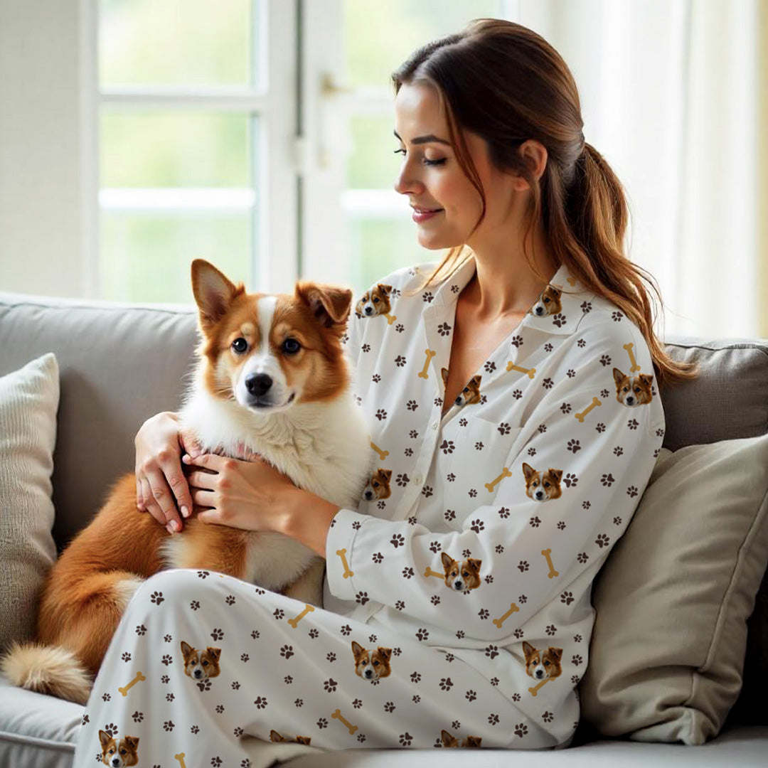 Vrouw met witte gepersonaliseerde pyjama met hondenprint, pootafdrukken en botten, houdt een bruin en witte hond op de bank vast
